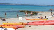 Varios kayak en primer plano y baistas al fondo en playa Es Copinyar 